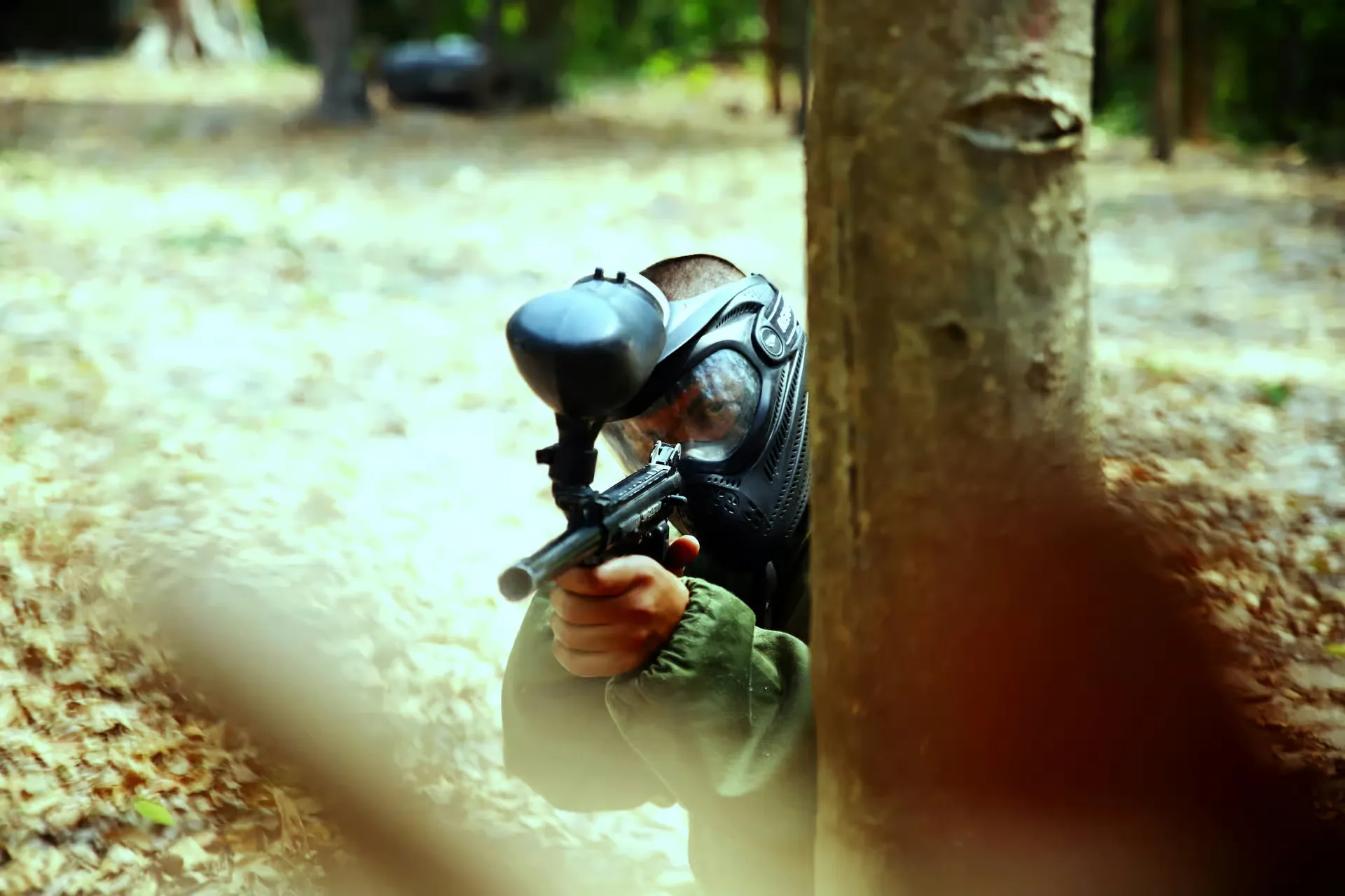 Paintball player aiming from behind a tree